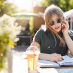 portrait-young-business-woman-student-writing-her-plans-notepad-talking-smartphone-wearing-glasses-luch-break-park-sunny-summer-day-copy-space_197531-30396